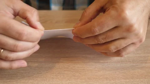 Person folding a white sheet of paper in half by hand on a wooden table in cl Stock Footage 341190377