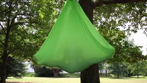 Person fully cocooned inside bright green aerial hammock gently swings under sum Stock Footage 313175740
