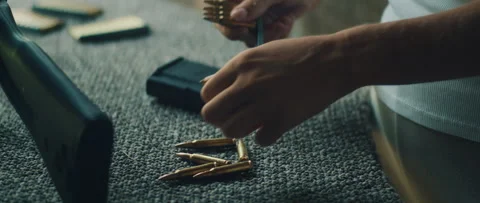 Person gathers bullets for magazine loading on bench during shooting preparation Stockbeeldmateriaal 311903366