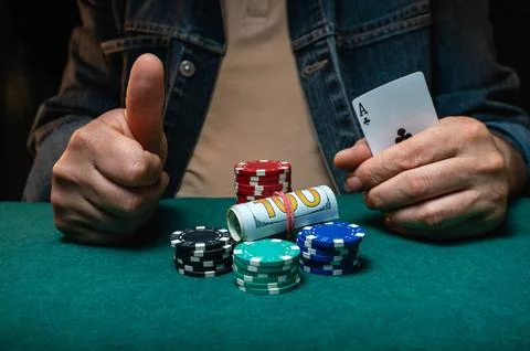 A person gives a thumbs up gesture while holding an ace card at a poker tab.. Stock Photos