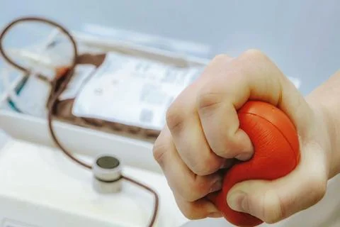 Person with gloved hand squeezing red stress ball while preparing for blood.. Stock Photos