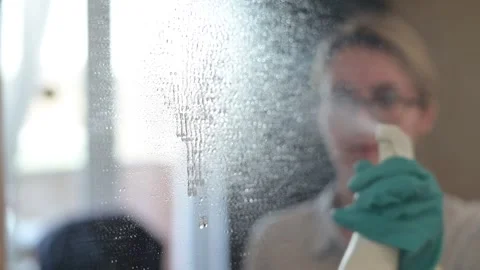 A person in gloves sprays cleaning solution onto a glass surface mirror, wiping Stock Footage 337555850