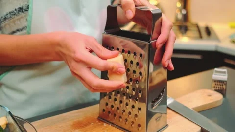 Person grating block cheese on a cutting board in modern kitchen Stockbeeldmateriaal 342888350