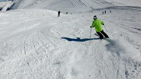 A person in a green jacket is skiing down a snow-covered slope, sunny day Stock Footage 330384244