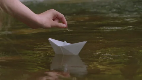 Person hand gently launching white paper boat on tranquil stream. Child han.. Video stock 342625424