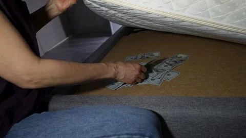 Person hand taking a bundle of US dollar bills hidden under a mattress Stock Footage 310007700