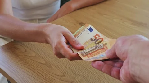 A person hands over a stack of banknotes to another individual at a wooden Stock Footage 346723672