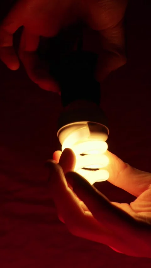 Person Hands Screw a Flickering Lightbulb Into a Socket Under Red Light Stock Footage 334136174
