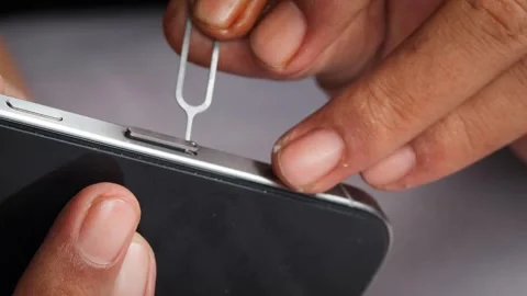 Person hands using an ejector tool to open the SIM card tray slot Stock Footage 348910164
