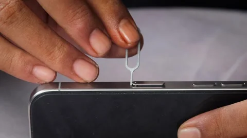 Person hands using an ejector tool to open the SIM card tray slot Stock Footage 348910178