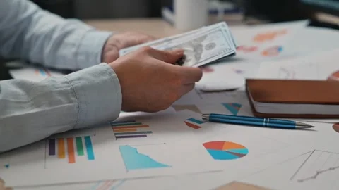 A person is holding banknotes while looking over various charts and graphs on a Stock-Footage 338301622
