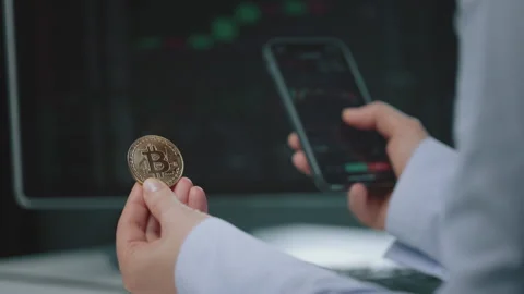 Person holding Bitcoin while checking market data on smartphone Stock Footage 328286206