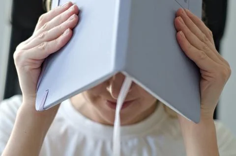 A person holding a book over their head, expressing frustration or stress Foto stock