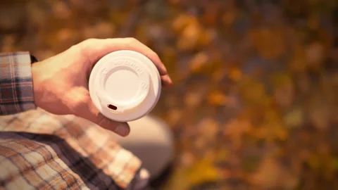 A person holding a coffee cup while enjoying a fall day in the park near col Stock Footage 291430974
