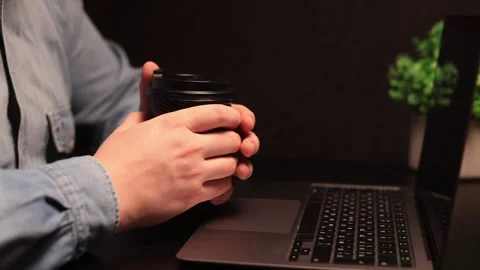 Person holding a coffee cup while working on a laptop with a plant in the Stock Footage 338432527