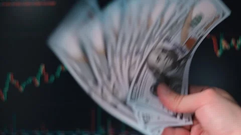 A person is holding dollar banknotes while looking at financial graphs in the 動画素材 338301420