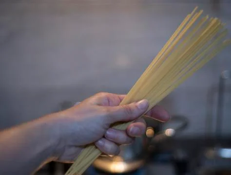 Person holding dried spaghetti in a kitchen Stock Photos