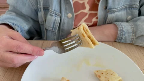 Person holding fork with piece of thin pancake over white plate  Video stock 342438052