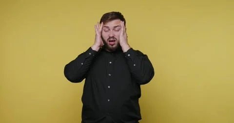 Person holding head in frustration while standing against a yellow backgrou.. Видео 326789860
