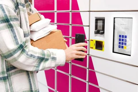 Person holding packages and using a smartphone at an automated parcel locke.. Foto stock