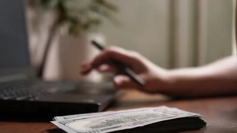 Person holding pen and using laptop touchpad with dollar bills stack Stock Footage 344058069