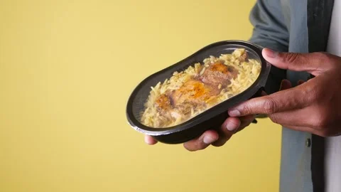 Person holding plastic container with chicken and rice meal against yellow .. Stock Footage 332199746