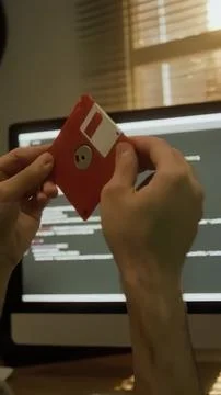 Person holding red floppy disk in front of computer screen 库存照片