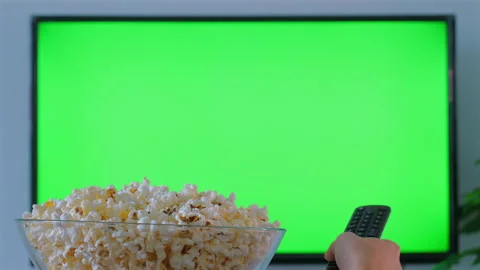 Person holding remote control and bowl of popcorn while watching TV Видео 284123647