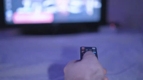 A person holding a remote control while watching television, with a blurry TV Stock Footage 276498559
