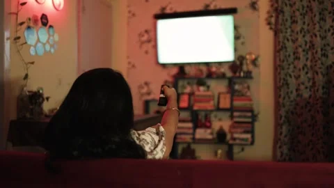 Person holding remote control while watching television in dimly lit living room Stock Footage 336405727