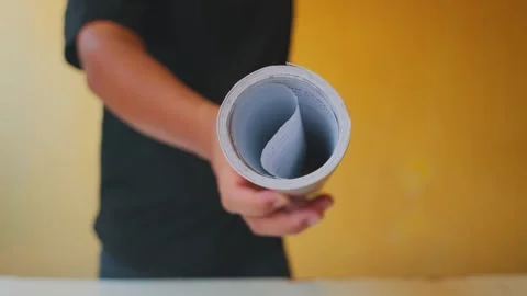 Person Holding a Rolled Document Against a Yellow Background Stock Footage 312503528