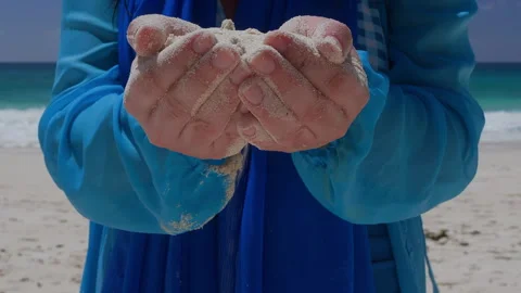 Person holding sand in cupped hands at beach wearing blue jacket Stock Footage 346368900