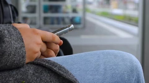 Person holding a smartphone while sitting on a station bench, with platform.. Video stock 328233347