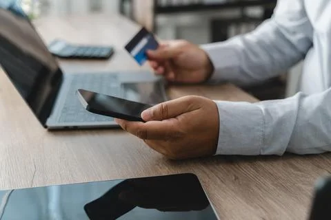 Person holding a smartphone while using a credit card and laptop for mobile.. Фото