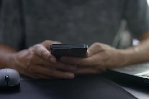 Person Holding Smartphone While Working at Desk with Laptop Mouse Stock Photos