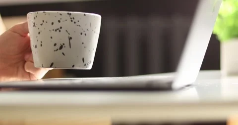 Person holding a speckled mug while working on a laptop at a desk Stock Footage 339074964