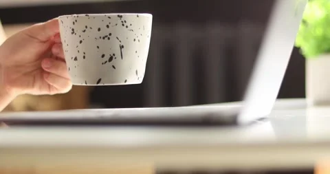Person holding a speckled mug while working on a laptop indoors Stock Footage 339075226