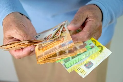 A person is holding a stack of euro banknotes in their hand. The bills are fo Stock Photos