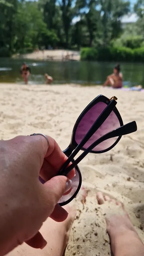 Person Holding Sunglasses While Relaxing on Sunny River Beach Stock Footage 339080915