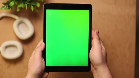 Person holding a tablet with a green screen and headphones nearby Vidéo 341737710