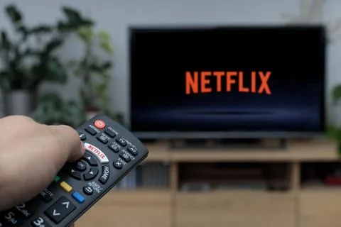 Person holding a TV remote controller displaying the Netflix logo with the Netfl Stock Photos