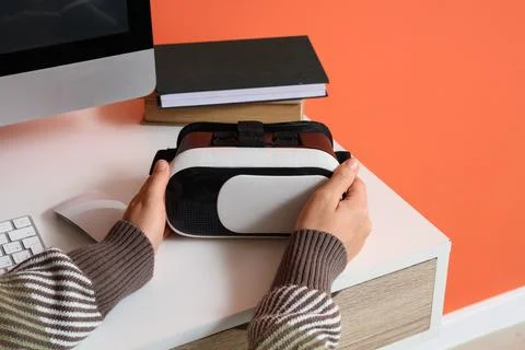 Person holding a virtual reality headset on a white desk with a computer moni Stock Photos