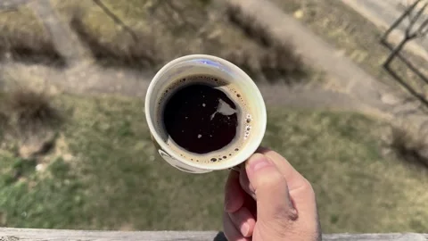A person holds a cup of coffee while standing on a balcony Stock Footage 332420522