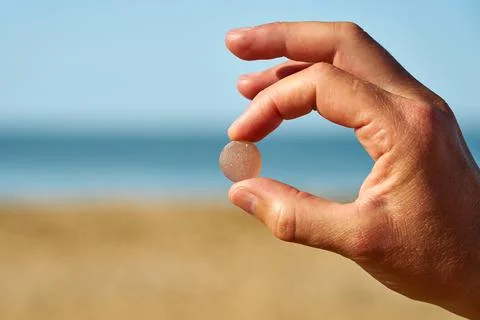 A person holds a single piece of pink sea glass between their finger and thumb Stock Photos