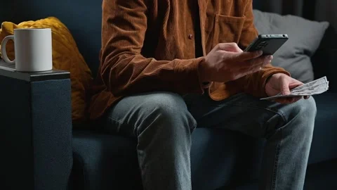 A person holds a smartphone while sitting on a couch in a living room. The Stock Footage 339097676