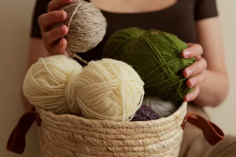 A person holds a soft white yarn above a basket that contains several different Stock Footage 336464863