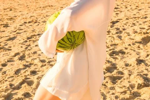 Person holds  watermelon while standing on the beach during sunset with soft Stock Photos