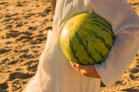 Person holds  watermelon while standing on the beach during sunset with soft Stock Photos
