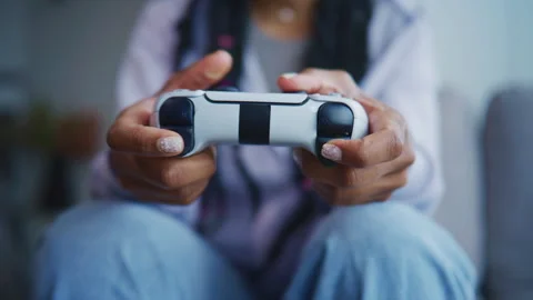 Person holds a white game controller while sitting on a couch in a living room d Stock Footage 339370372