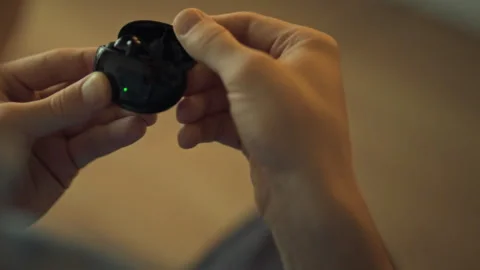 Person holds a wireless earbud case while preparing to use it indoors Stock Footage 323869270